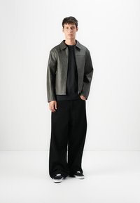 Gray leather jacket with a collar, zip closure, and subtle texture; paired with black wide-leg trousers and black sneakers.