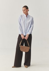 Light blue button-up shirt with a band collar, paired with black wide-leg trousers. Holding a brown suede handbag. Pointed beige shoes.