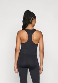 Μαύρο αθλητικό εσώρουχο με σχέδιο racerback, φτιαγμένο από λείο ύφασμα. Το κάτω μέρος φτάνει στη μέση, συμπληρώνοντας αντίστοιχες κολάν.