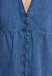 Denimové šaty s hlubokým výstřihem do V, předním zapínáním na kulaté textilní knoflíky a nařaseným pasem. Barva je tmavě modrá.