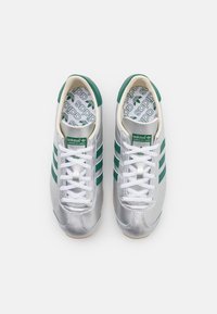Pair of silver Adidas sneakers with green stripes and logo, white laces, and branded insoles, viewed from above on a white background.