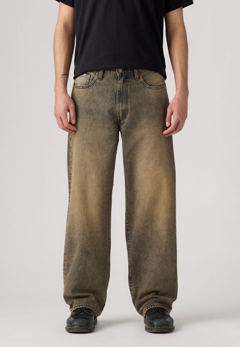 Χαλαρά, ξεθωριασμένα τζιν σε ανοιχτό καφέ απόχρωση με πιο σκούρες λεπτομέρειες. Σχεδίαση με πέντε τσέπες, ορατές ραφές και κανονική γραμμή στα πόδια.