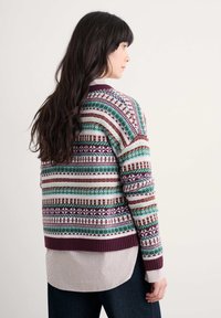 Knit sweater with multicolored geometric patterns in maroon, green, and blue; ribbed cuffs and hem. Layered over a striped collared shirt.