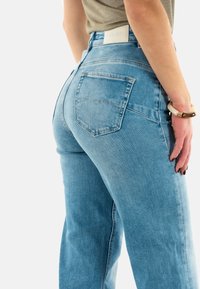 Jeans de tiro alto en azul claro con una silueta ajustada, dos bolsillos traseros y un ligero desgastado. Fabricados en denim con una ligera textura.