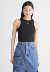 Black ribbed tank top featuring a blue "HUGO" logo, paired with a high-waisted denim skirt with pockets and a button closure.