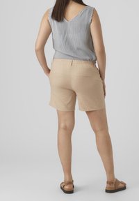 Pantalones cortos de algodón beige con una cintura elástica, de largo hasta la rodilla, combinados con una blusa sin mangas de rayas blancas y negras. Sandalias con un detalle de hebilla.