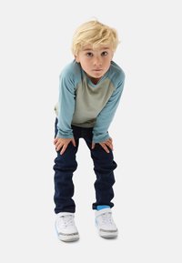 Langærmet lyseblå og grå skjorte med raglanærmer, mørk denim jeans og hvide sneakers med blå accenter og mønstrede detaljer.