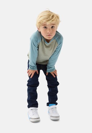Langärmliges hellblaues und graues Hemd mit Raglanärmeln, dunkelblaue Jeans und weiße Turnschuhe mit blauen Akzenten und gemusterten Details.