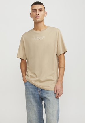Beige bomuld t-shirt med korte ærmer, rund halsudskæring, med teksten "JACK & JONES PREMIUM" i hvidt på brystet.