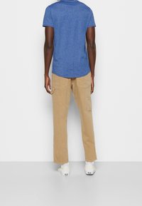 Camisa azul de manga corta con cuello redondo combinada con pantalones de cargo beige que tienen bolsillos laterales. Diseño sencillo y casual, llevada con zapatos blancos.