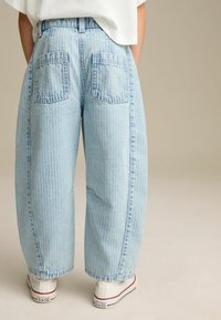Jean large bleu clair avec des rayures blanches verticales, dotés de deux poches arrière et d'une taille haute, associés à des chaussures en toile blanches.