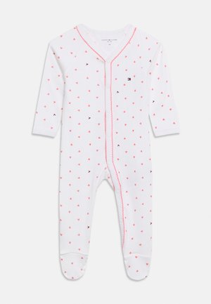 Weißer Baby-Strampler mit langen Ärmeln und Füßchen, bedeckt mit kleinen pinkfarbenen Herzen, pinkfarbener Einfassung entlang der Druckknöpfe vorne und winzigen dunkelblauen Logos.