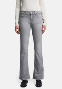 Grå flared jeans lavet af denim, med frynset kant og forlommer. Kombineret med en lys striktrøje og sorte sko.