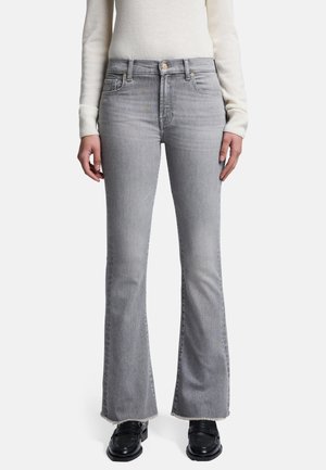 Grå flared jeans lavet af denim, med frynset kant og forlommer. Kombineret med en lys striktrøje og sorte sko.