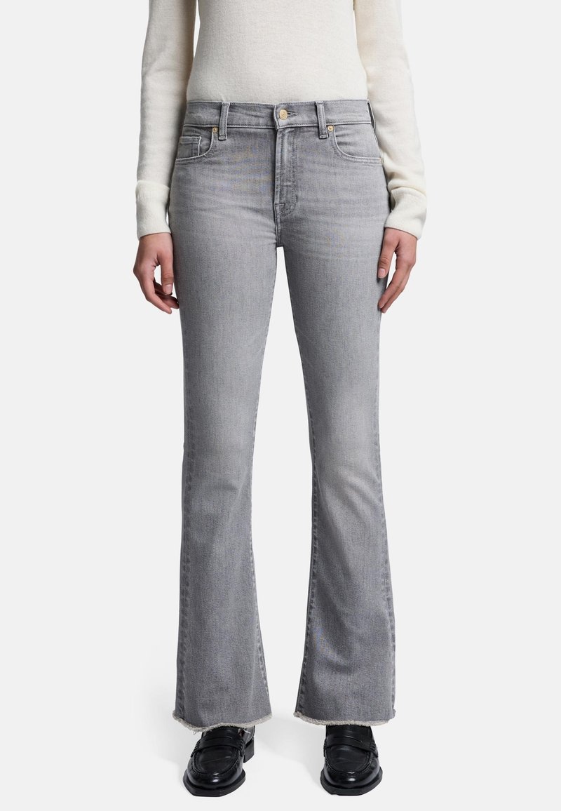 Grå flared jeans lavet af denim, med frynset kant og forlommer. Kombineret med en lys striktrøje og sorte sko.