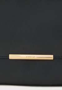 Čierna kožená kabelka s hladkou textúrou a kovovým zlatým detailom s vyrazeným názvom značky "Furla" na zapínaní.