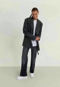 Gray checkered oversized blazer with long sleeves, paired with a white t-shirt and dark wide-leg jeans. Styled with white sneakers.
