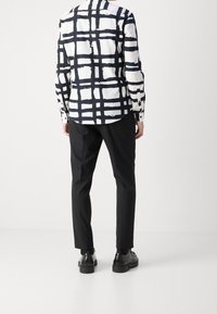 Chemise blanche avec motif à carreaux en forme de coups de pinceau noirs, associée à un pantalon noir. Dispose de poignets boutonnés et d'un ourlet incurvé. Des chaussures noires sont portées.