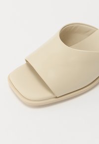 Sandale beige à bout ouvert avec large bride croisée et design carré à l’avant sur fond blanc.