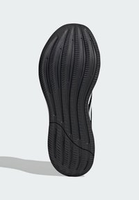 Schwarze Gummisohle mit strukturierten Rillen und Erhebungen, die eine geschwungene Silhouette aufweist und kontrastierende weiße Akzente an der Seite hat.