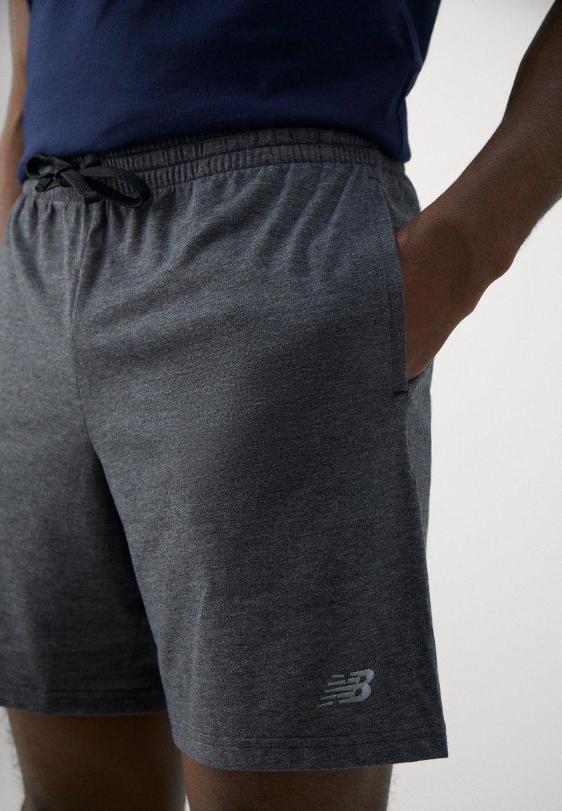 Shorts de sport gris en matériau doux, avec une taille élastique dotée d'un cordon de serrage et des poches latérales. Logo New Balance sur l'ourlet inférieur.