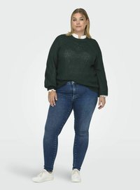 Pulover tricotat de culoare verde închis, cu o croială lejeră și un model texturat, purtat peste blugi albaștri cu talie înaltă. Asortat cu teniși albi.