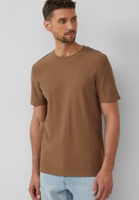 Braunes geripptes T-Shirt mit Rundhalsausschnitt und kurzen Ärmeln. Der Stoff wirkt weich mit einer dezenten Textur und wird mit hellblauen Jeans kombiniert.