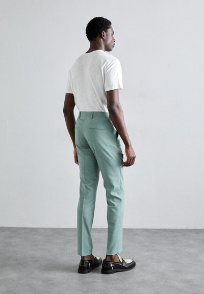 Calças ajustadas verde menta combinadas com uma t-shirt branca texturada e sapatos pretos brilhantes com detalhes em verde e amarelo.