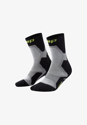 Calzini sportivi neri e grigi a girocchi con testo giallo-verde e imbottitura rinforzata nelle zone del tallone e delle dita su uno sfondo bianco.