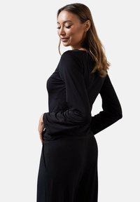 Czarna damska bluzka z długim rękawem o dopasowanym kroju. Wyróżnia się miękką fakturą, rękawami w kształcie dzwonu oraz okrągłym dekoltem.