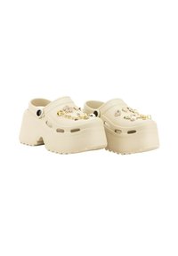 Zuecos de plataforma beige hechos de material ligero, con charms decorativos y una superficie texturizada, además de orificios de ventilación y una suela gruesa.