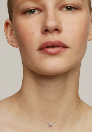 Collar de plata con un pequeño colgante redondo que presenta un diseño floral. La cadena es delicada, complementando el estilo minimalista.