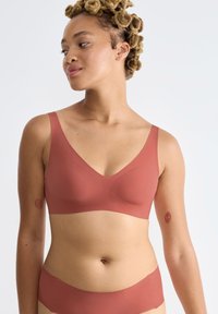 Różowo-brązowy biustonosz bezszwowy z szerokimi ramiączkami i dekoltem w kształcie litery V, wykonany z miękkiego, elastycznego materiału. Modelka nosi pasujące majtki bikini.