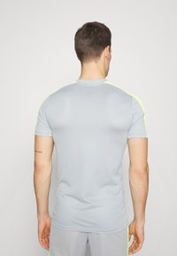 Camiseta atlética gris de manga corta, con tejido texturizado y brillantes acentos en neón amarillo en los hombros.