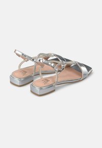 Zilveren platte sandalen met een puntige neus. Beschikt over kruislings gespen en metalen elementen. Textured voetbed en chunky zolen.