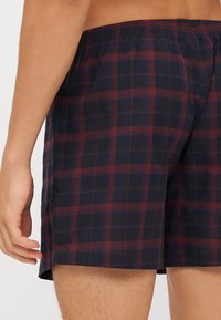 Rutete badetights i marineblå og bourgogne med elastisk linning. Har en sidelomme for enkel bevegelse, laget av lett materiale.