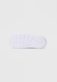 Semelle de chaussure de sport blanche avec des rainures texturées et un motif circulaire ; présente un logo Nike au talon et un matériau en caoutchouc lisse.