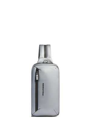 Sac bandoulière fin gris argenté avec poche zippée verticale sur le devant et une sangle rembourrée unique, debout sur un fond blanc.