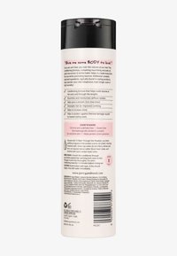Witte fles met een zwarte flip-top dop bevat tekst over een conditionerformule voor haar, met details over ingrediënten en voordelen op de achterkant.