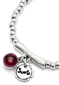 Bracelet en perles argentées avec un fermoir à bascule, mettant en avant une pierre précieuse rouge ronde et un charm circulaire gravé de "Suerte".