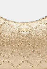 Borsa in pelle dorata con motivo impresso che presenta il nome del marchio, LUI.JO, e una texture liscia. Parte superiore arcuata con una forma strutturata.
