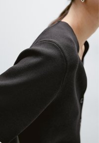 Zwarte gebreide cardigan met een ronde halslijn, knopen aan de voorkant, een ontspannen pasvorm, gestructureerde schoudernaden en een gladde textuur.