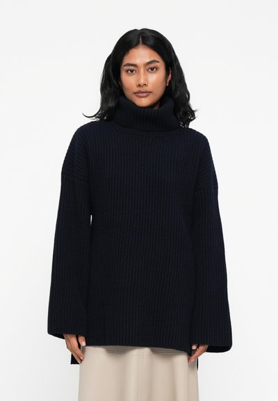 Marineblauwe geribbeld gebreide coltrui met brede mouwen en zijsplitsen. Zachte textuur en een relaxed fit, ontworpen voor comfort en warmte.