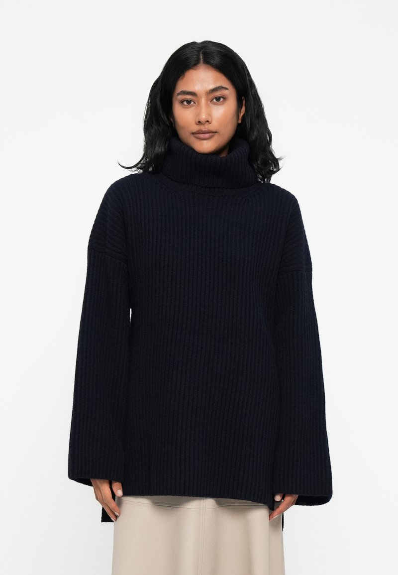 Mornarska rebrasta pletena turtleneck pulover z širokimi rokavi in stranskimi razporki. Mehka tekstura in sproščen kroj, zasnovan za udobje in toploto.