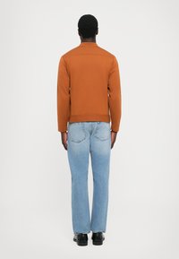 Chaqueta de algodón marrón con corte recto, combinada con jeans rectos de color azul claro. Textura suave, diseño minimalista y sin acentos visibles.