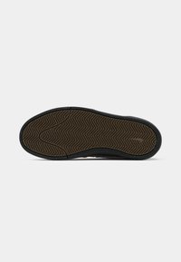 Sohle eines schwarz-braunen Sneakers mit einem strukturierten Zickzack-Profil auf einem weißen Hintergrund.