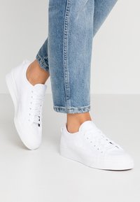 Vita sneakers av canvas med rund tå, snörning fram och texturerad ovandel. Har en vit platåsula och diskret logodetalj på sidan.