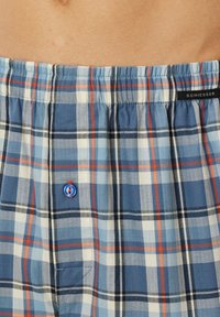 Boxer da uomo a quadri blu e bianchi realizzati in un tessuto morbido, con una cintura elastica e un piccolo bottone blu sul davanti.