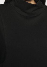 Czarny golf z miękką, gładką teksturą; posiada wysoki kołnierz i krótkie rękawy, prezentując prosty, minimalistyczny design.