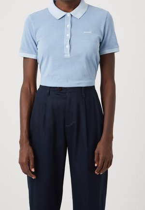 Lichtblauw poloshirt met korte mouwen en witte knopen, ingestopt in donkernavy plisseren broek met hoge taille, gedragen door een persoon.